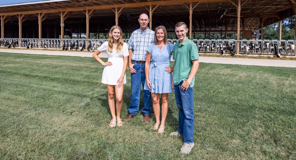 A family pose in front of their barn with cows