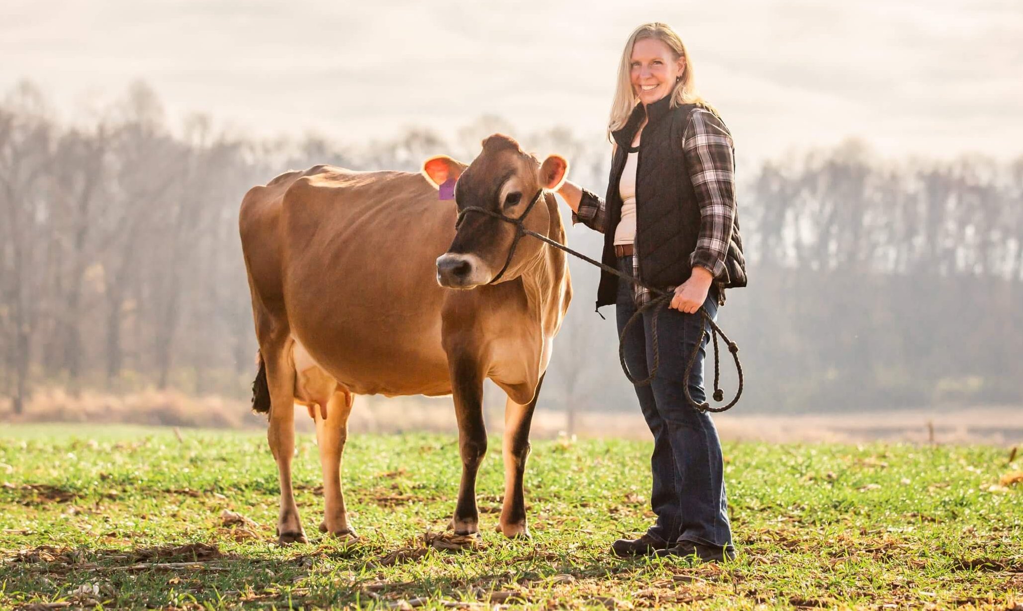 a woman stands with her cow in the field